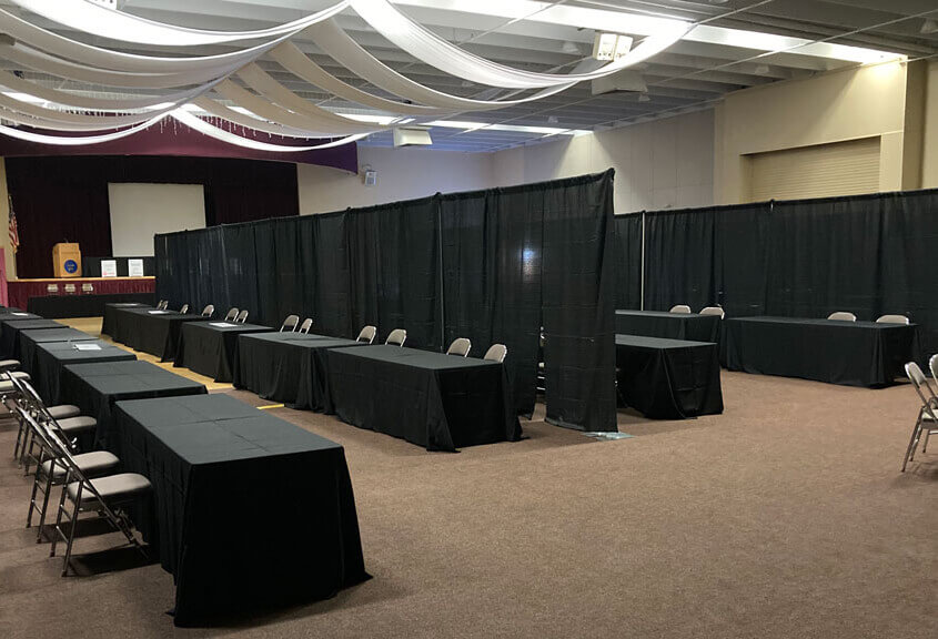 Trade-Show-Black-Banjo-Drape-In-Multiple-Rows-With-Tables-And-Chairs-for-Rent